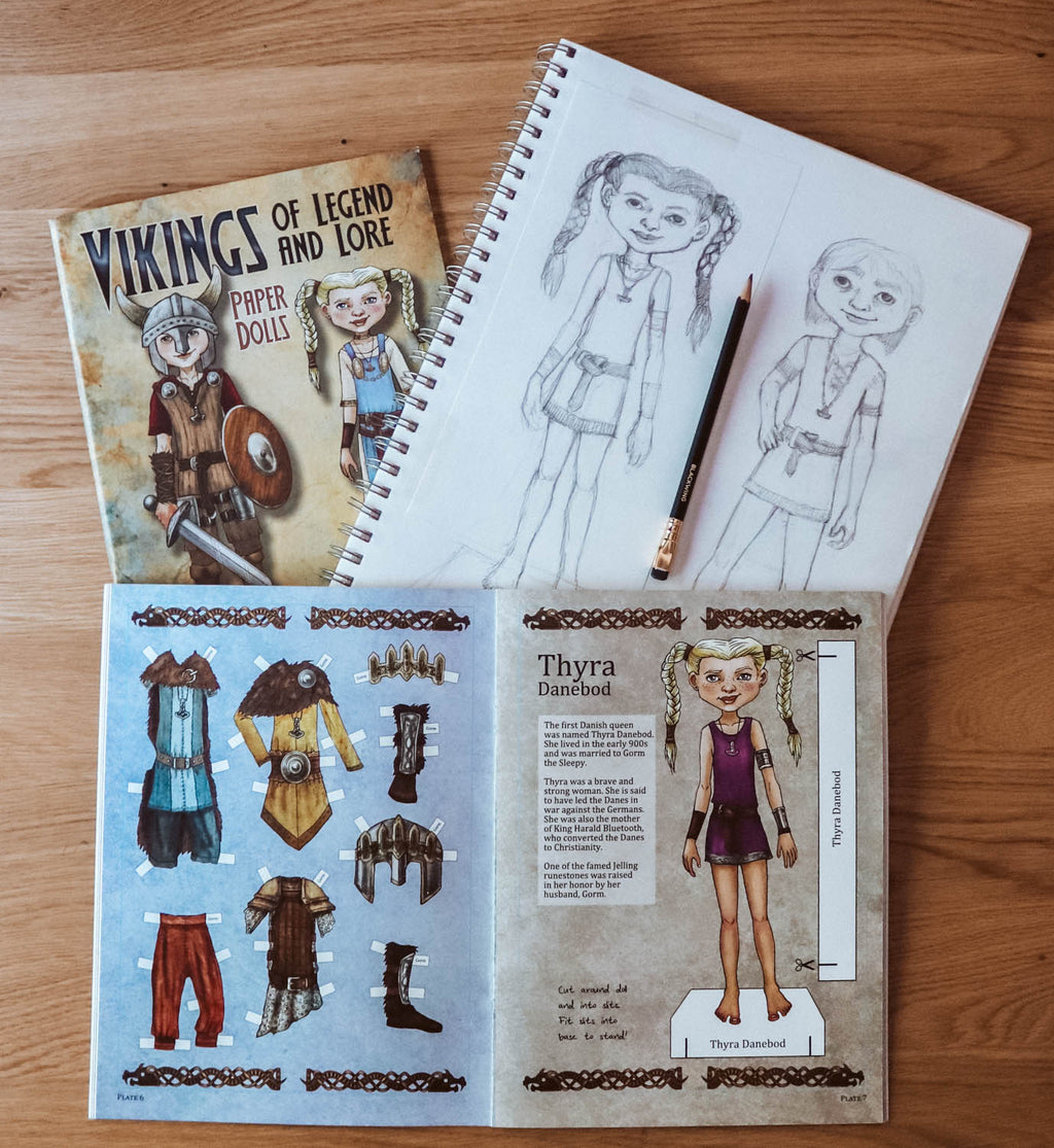 A children's craft activity book titled 'Vikings of Legend and Lore' shown with a spiral sketchbook, pencil, and an open page featuring a character sheet and outfit cutouts, all arranged on a wooden surface.