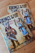 Two copies of the book 'Vikings of Legend and Lore: Paper Dolls' by Kiri Oestergaard Leonard, featuring illustrated Viking characters on the cover, displayed on a light wooden surface.