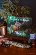 A square art print or canvas titled "The Year of the Unicorn" displayed on a wooden easel. The artwork depicts a unicorn in a forest with the year 2018 overlaid.