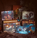 A styled flat-lay of four illustrated greeting cards featuring fantasy woodland characters, arranged on vintage-style books with pine branches, nuts, and a dark textured fabric background.