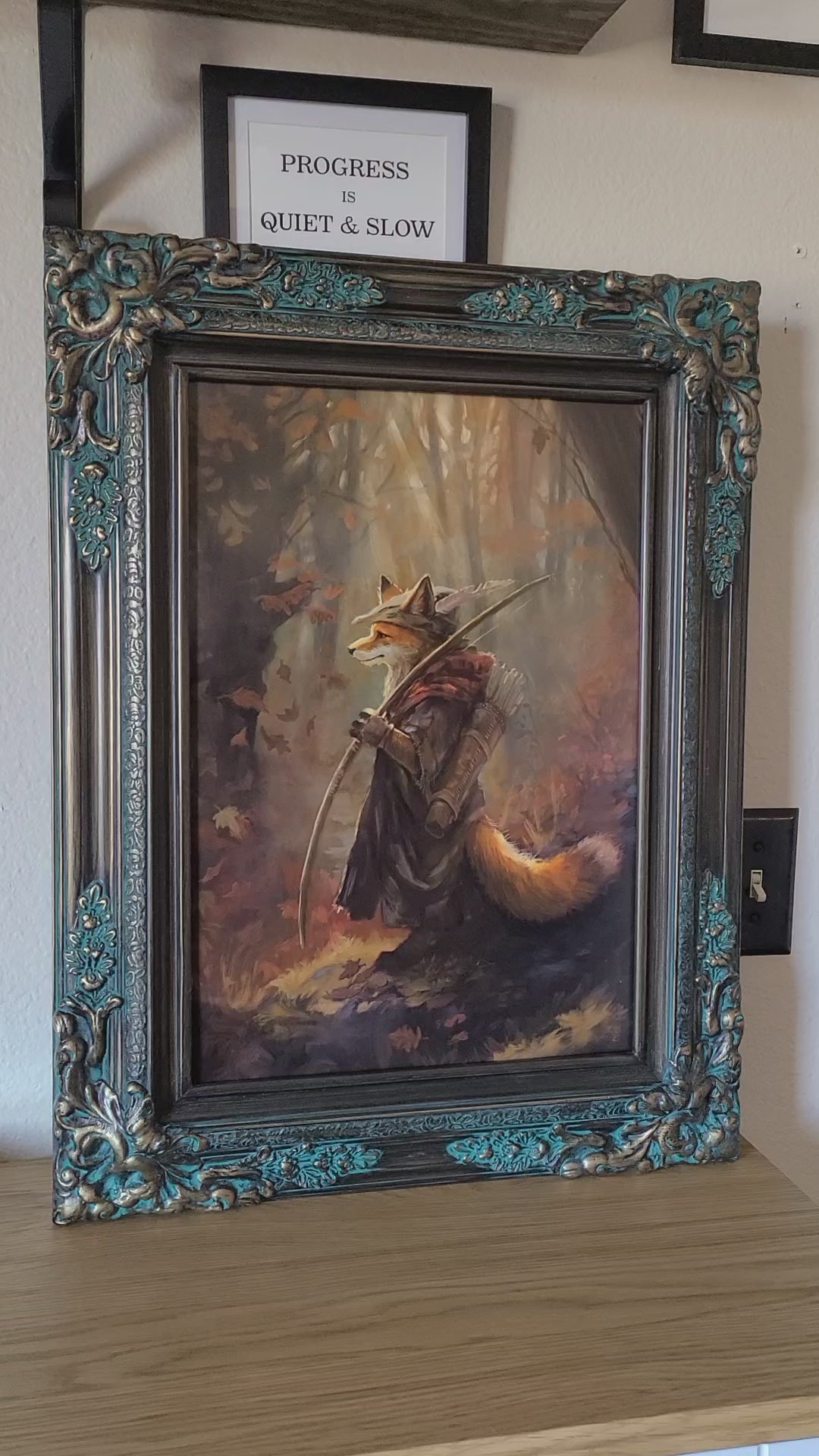 A short video showing an art print of a digital painting with a Robin Hood like fox in a forest setting. The art print is framed in an ornate brass and green frame.