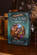 The Green Witch Tarot card deck box by Ann Moura, styled on a wooden table with candles and dried flowers in the background.