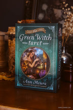 The Green Witch Tarot card deck box by Ann Moura, styled on a wooden table with candles and dried flowers in the background.