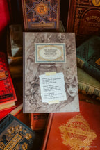 A sketchbook titled The Heretofore Undisclosed sketchbook of Subject 1984 written by Kiri Oestergaard Leonard surrounded by vintage red and gold-bound books.